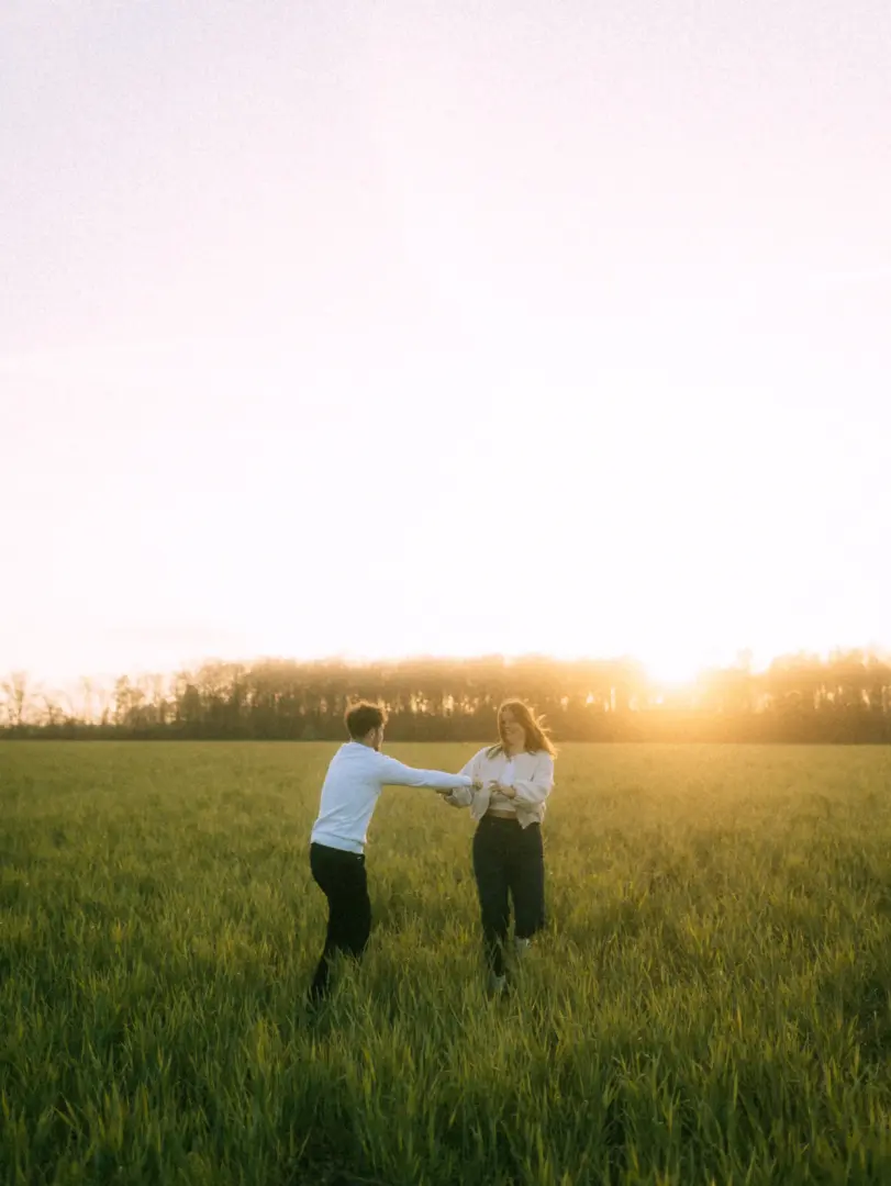 Ein junges Paar hält sich an den Händen und läuft lachend durch ein grünes Feld während des goldenen Sonnenuntergangs. Diese authentischen Pärchenfotos in Schwerin fangen die romantische Stimmung und die natürliche Verbundenheit der beiden in einer warmen Lichtstimmung ein.