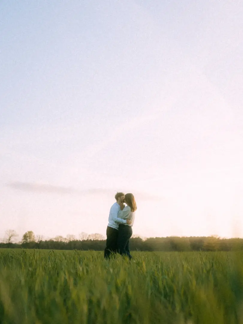 Ein verliebtes Paar steht sich in einem weiten, grünen Grasfeld gegenüber und küsst sich zärtlich im warmen Licht der Abendsonne. Die romantische Atmosphäre unterstreicht ihre Verbundenheit bei einem professionellen Shooting für Pärchenfotos in Schwerin.