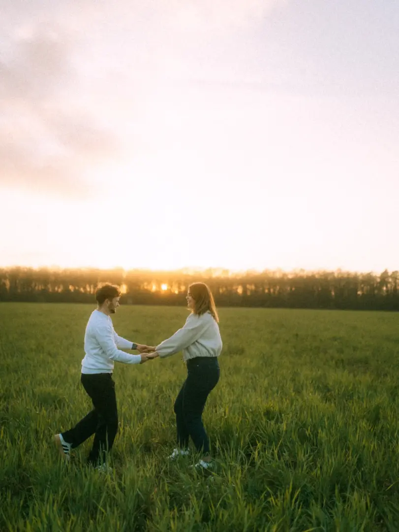 Ein junges Paar hält sich bei Sonnenuntergang glücklich an den Händen und dreht sich auf einer grünen Wiese, eingefangen bei einem romantischen Fotoshooting für Pärchenfotos in Schwerin.