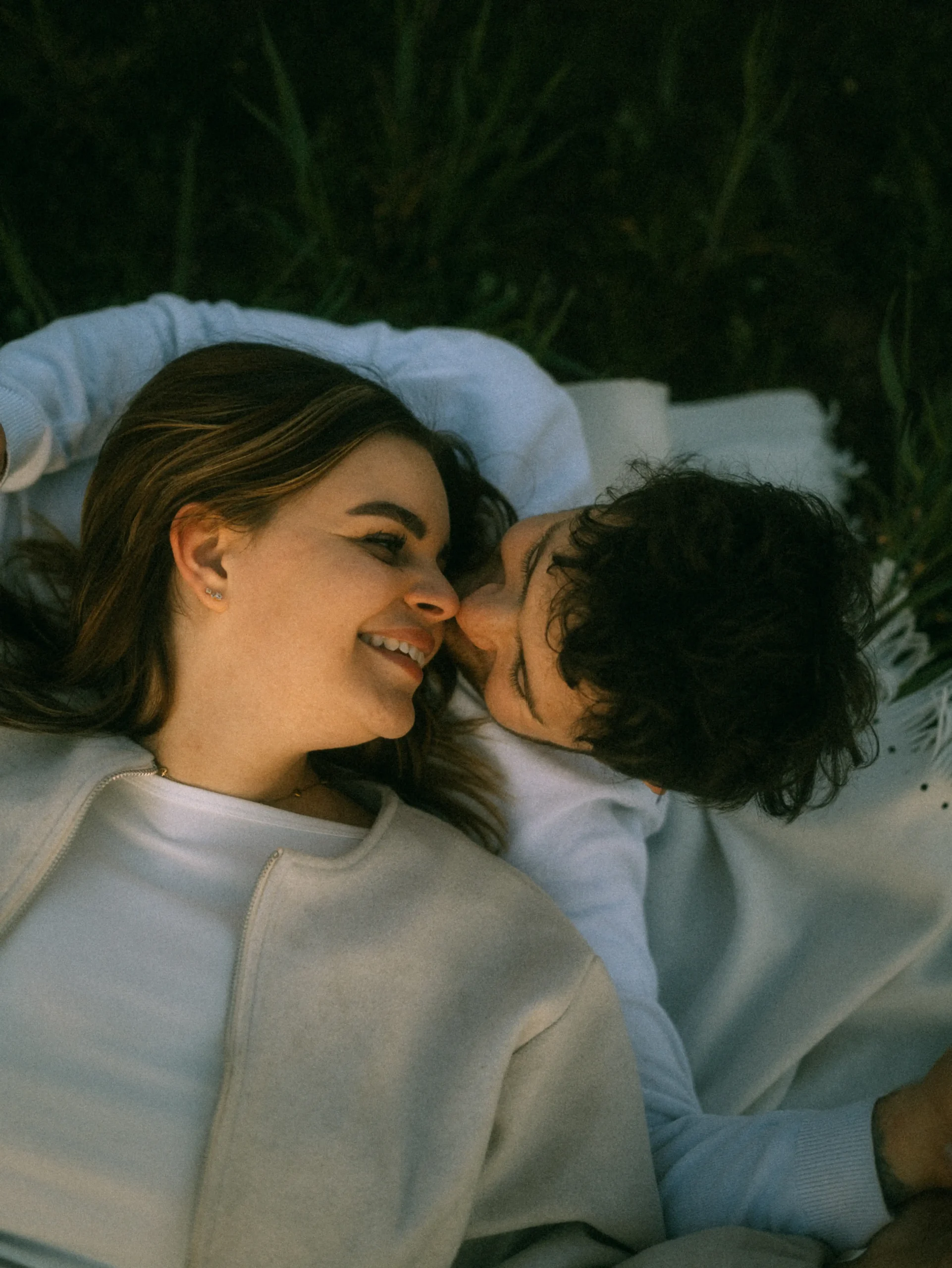Glückliches Paar liegt auf einer Decke im Gras, Mann küsst die Frau auf die Wange, Lovestory Fotograf in Schwerin und MV.