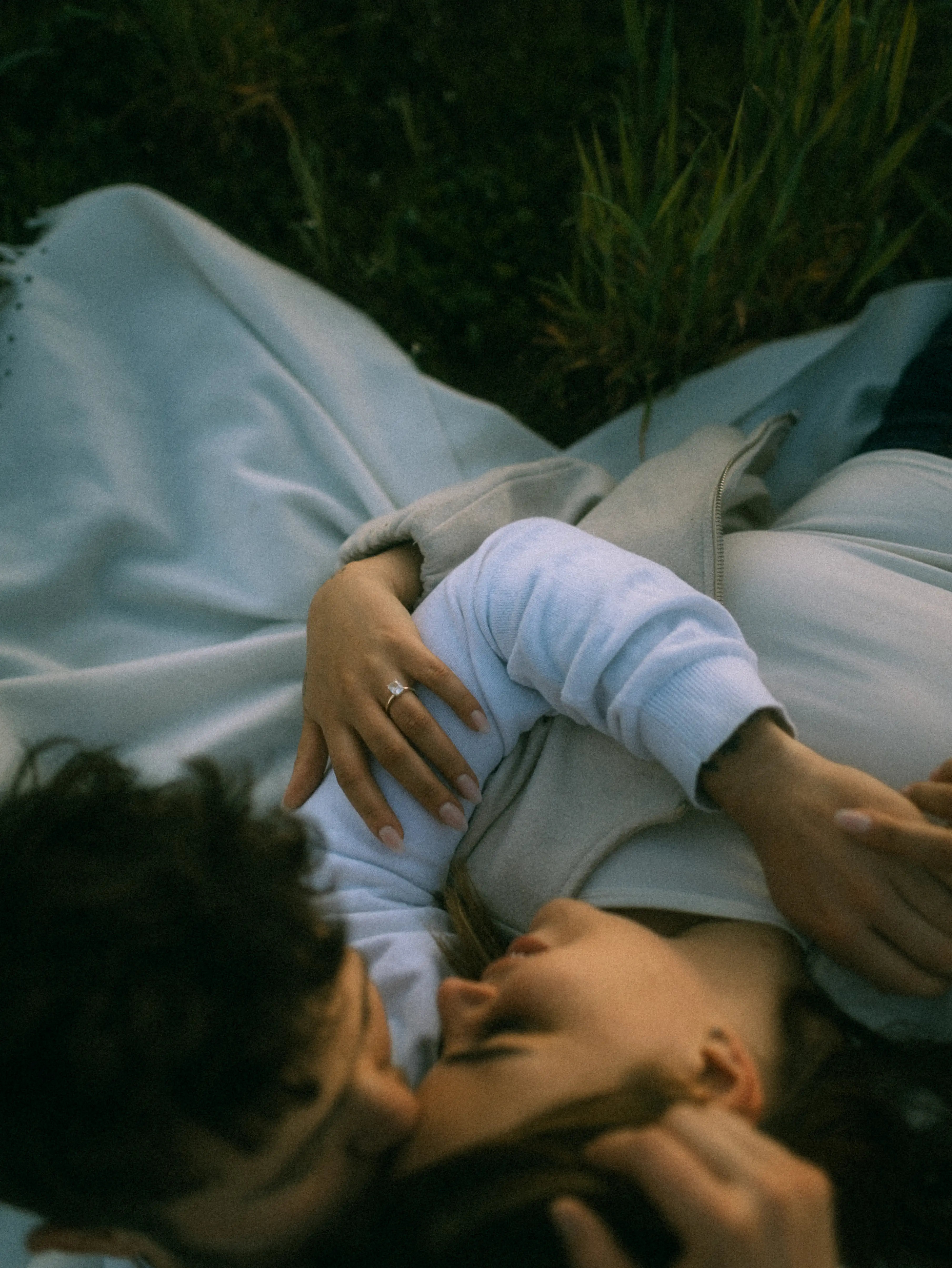 Ein junges Paar liegt eng umschlungen im Gras, die Frau trägt einen Ring, der auf eine Verlobung oder Hochzeit hindeutet. Romantische Lovestory in Mecklenburg-Vorpommern.