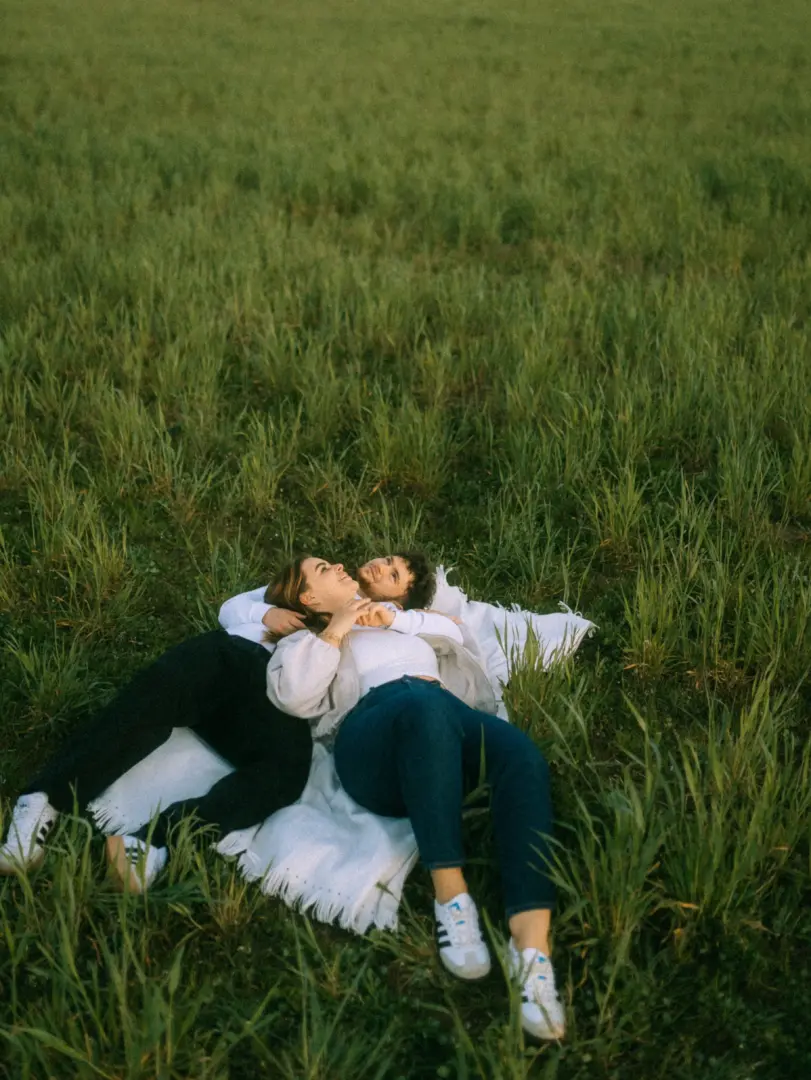 Ein verliebtes Paar liegt entspannt auf einer hellen Decke in einer grünen Wiese und genießt den Moment bei einem gemütlichen Picknick. Die authentischen Pärchenfotos in Schwerin fangen die romantische Stimmung und die Verbundenheit der beiden perfekt ein.