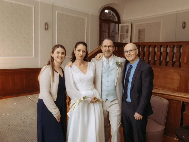 Ein glückliches Brautpaar posiert nach der Trauung gemeinsam mit zwei Gästen in einem eleganten historischen Gebäude. Das Foto wurde von einem Hochzeitsfotograf in Schwerin und MV aufgenommen und zeigt die festliche Stimmung in einem Raum mit Holzgeländer und klassischer Architektur.