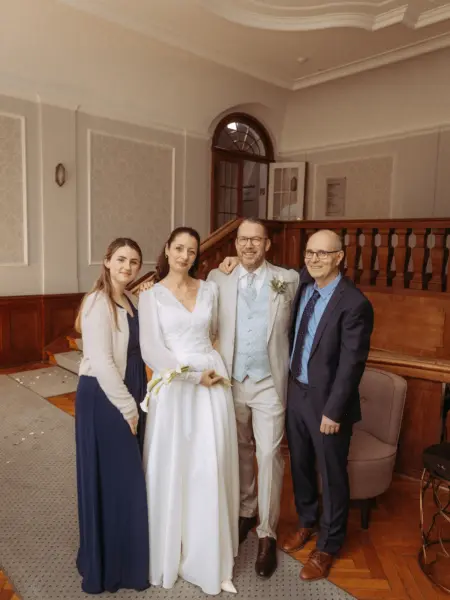 Das Brautpaar posiert nach der Zeremonie strahlend mit zwei Gästen vor einer historischen Holztreppe in einem eleganten Innenraum. Diese Aufnahme wurde von einem Hochzeitsfotograf in Schwerin und MV festgehalten, der die festliche Stimmung und die stilvolle Architektur einfängt.