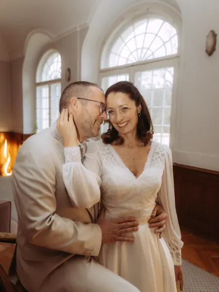 Ein glückliches Brautpaar in einem hellen, eleganten Saal mit großen Bogenfenstern. Die Braut trägt ein weißes Spitzenkleid, der Bräutigam einen hellen Anzug. Eine romantische Momentaufnahme von Ihrem Lovestory Fotograf in Schwerin und MV.