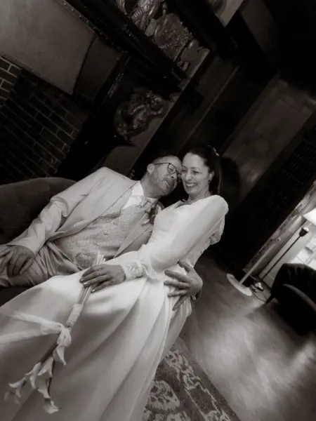 Ein glückliches Brautpaar in einem eleganten Interieur: Die Braut sitzt auf dem Schoß ihres Bräutigams, während beide liebevoll miteinander lachen. Eine romantische Aufnahme vom Lovestory Fotograf in Schwerin und MV, die eine intime und herzliche Stimmung einfängt.