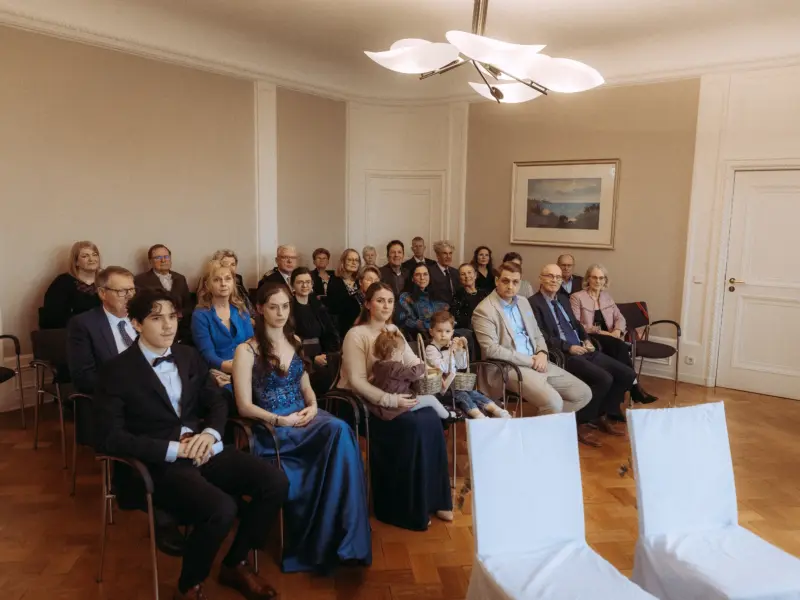 Gäste bei einer feierlichen Trauung in einem hellen, eleganten Saal. Hochzeitsfotograf in Schwerin und MV. Die Hochzeitsgesellschaft sitzt in Reihen auf Stühlen und wartet auf das Brautpaar, während zwei weiße Stühle im Vordergrund auf die Zeremonie hindeuten.