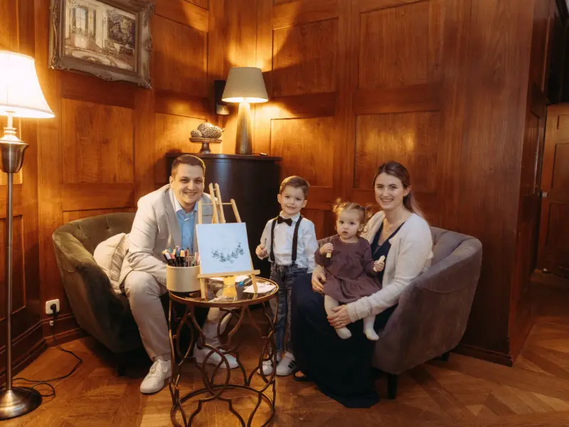 Eine glückliche Familie posiert in einem eleganten, holzgetäfelten Raum für ein Familienfotos in Schwerin. Vater, Mutter und ihre zwei Kinder sitzen auf gemütlichen Sesseln neben einer Staffelei mit der Aufschrift „Wedding Guest Book“. Ein professioneller Familienfotograf in Schwerin.