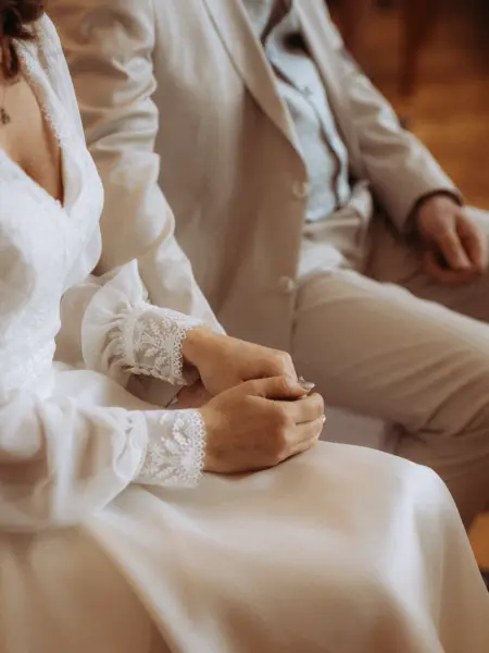 Nahaufnahme eines Brautpaares, bei dem sich die Braut in einem eleganten weißen Kleid mit Spitzenärmeln sanft die Hände hält, während sie neben ihrem Bräutigam im hellen Anzug sitzt – ein emotionaler Moment eingefangen von einem Hochzeitsfotograf in Schwerin und MV.