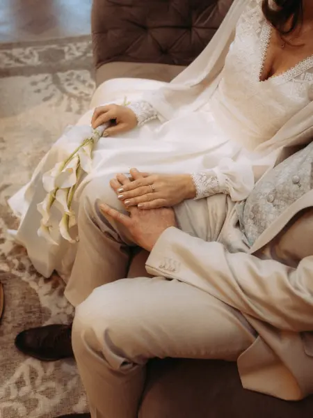 Ein Brautpaar hält sich zärtlich an den Händen, während die Braut einen Strauß aus weißen Calla-Lilien trägt. Ihr elegantes weißes Kleid mit Spitzenärmeln harmoniert mit dem hellen Anzug des Bräutigams. Ein stimmungsvoller Moment, eingefangen von Ihrem Lovestory Fotograf in Schwerin und MV.