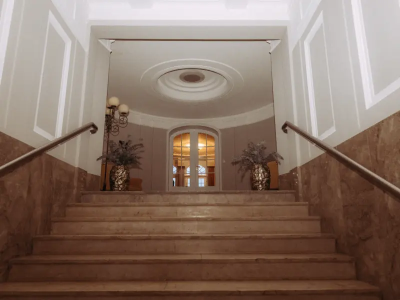 Elegante, mit Marmor verkleidete Treppe in einem historischen Gebäude mit klassischer Architektur, die zu einer hell erleuchteten Doppeltür führt. Ein stimmungsvolles Ambiente für Paare, festgehalten von Ihrem Hochzeitsfotograf in Schwerin und MV.