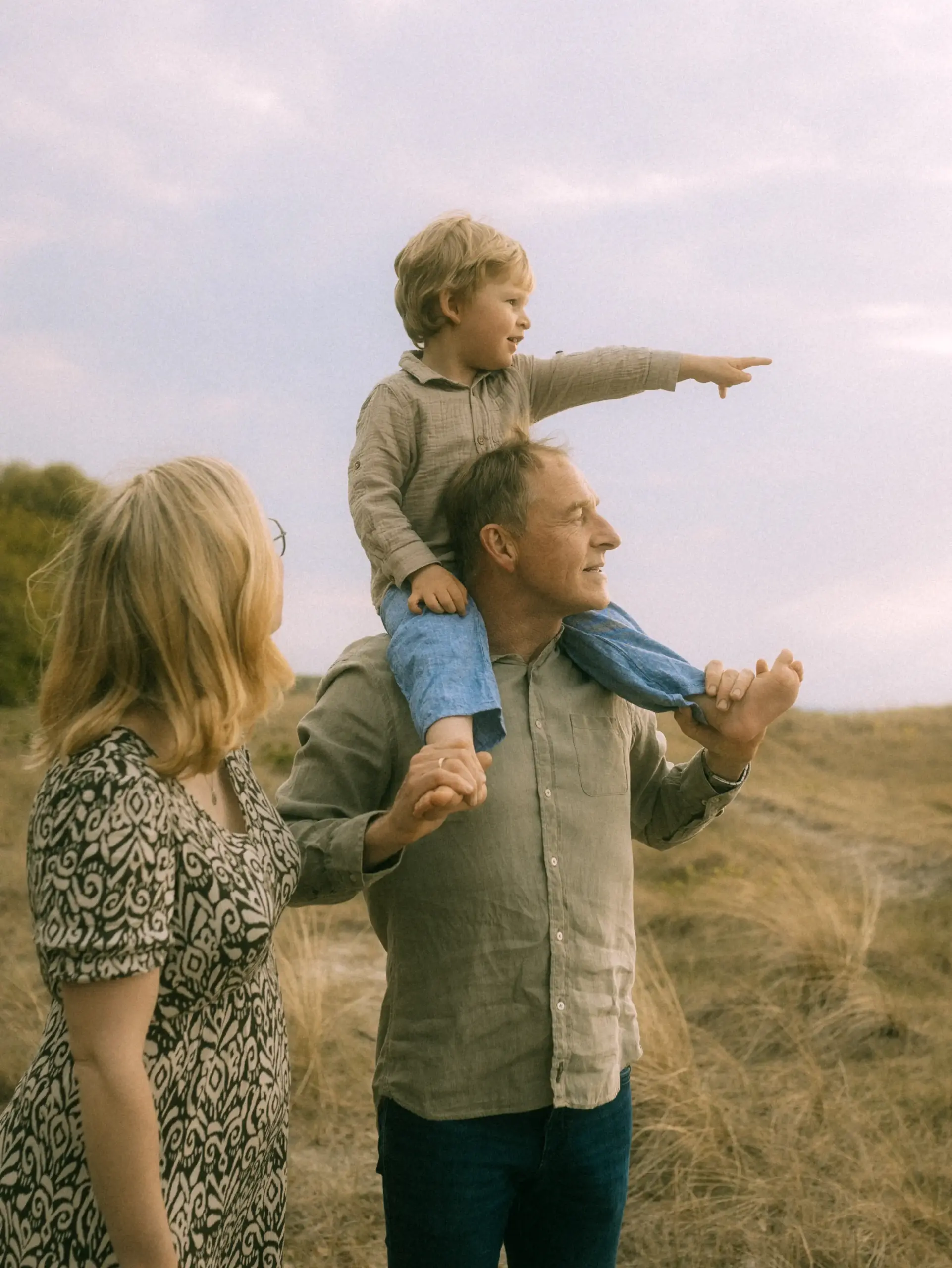 Ein glücklicher Großvater trägt sein Enkelkind auf den Schultern durch eine herbstliche Wiesenlandschaft, während die Großmutter daneben läuft. Ein herzlicher Moment, eingefangen von einem Familienfotograf in Schwerin bei einem entspannten Familienshooting in der Natur.