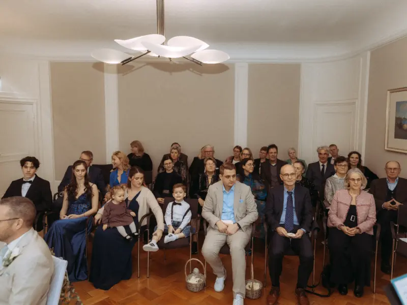 Eine Hochzeitsgesellschaft sitzt in einem eleganten Raum während einer Zeremonie. Gäste in festlicher Kleidung blicken aufmerksam nach vorn, während ein Hochzeitsfotograf in Schwerin und MV diesen feierlichen Moment einfängt. Das Ambiente ist geprägt von zeitloser Eleganz.