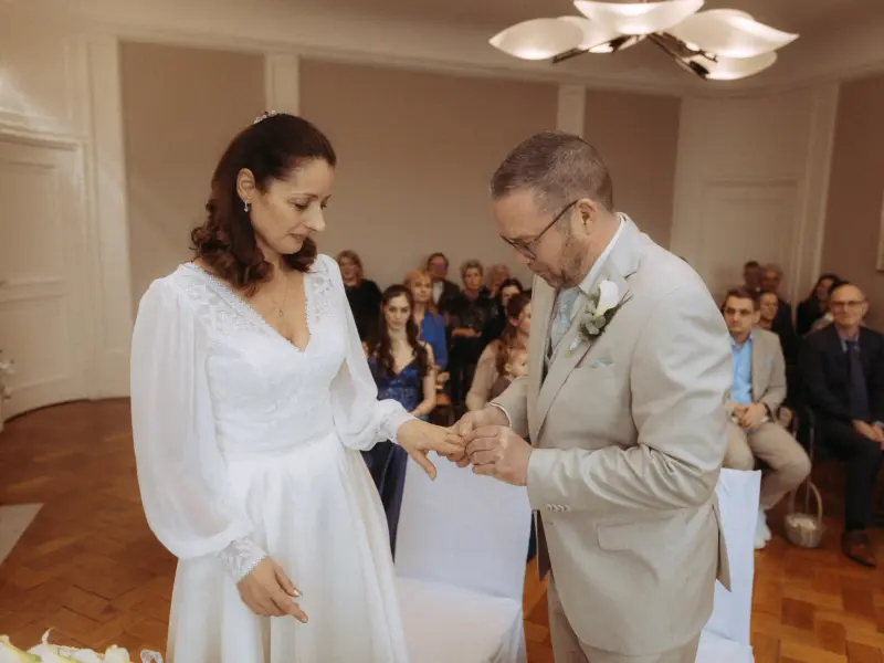 Ein Brautpaar bei der feierlichen Ringübergabe während der Trauung in einem eleganten Saal. Die Braut trägt ein weißes Kleid mit Spitzenbesatz, der Bräutigam einen beigen Anzug. Ein emotionaler Moment, festgehalten von einem Hochzeitsfotograf in Schwerin und MV.