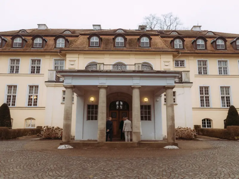 Ein elegantes Herrenhaus im neoklassizistischen Stil mit einem imposanten Säulenportal, vor dem drei Männer in Anzügen stehen, aufgenommen von einem Hochzeitsfotograf in Schwerin und MV.