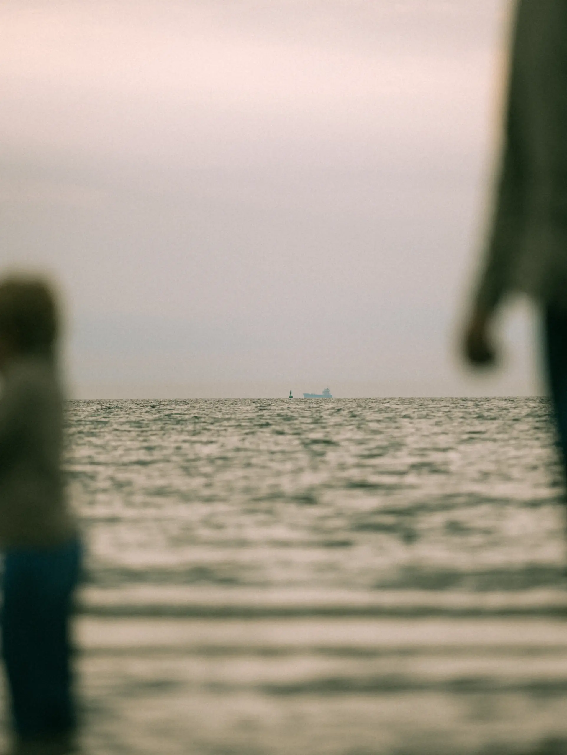 Ein unscharfer Familienfotograf in Schwerin hält den Blick auf das weite Meer fest, während im Hintergrund ein kleines Schiff und eine Boje am Horizont unter einem bewölkten Himmel zu sehen sind.