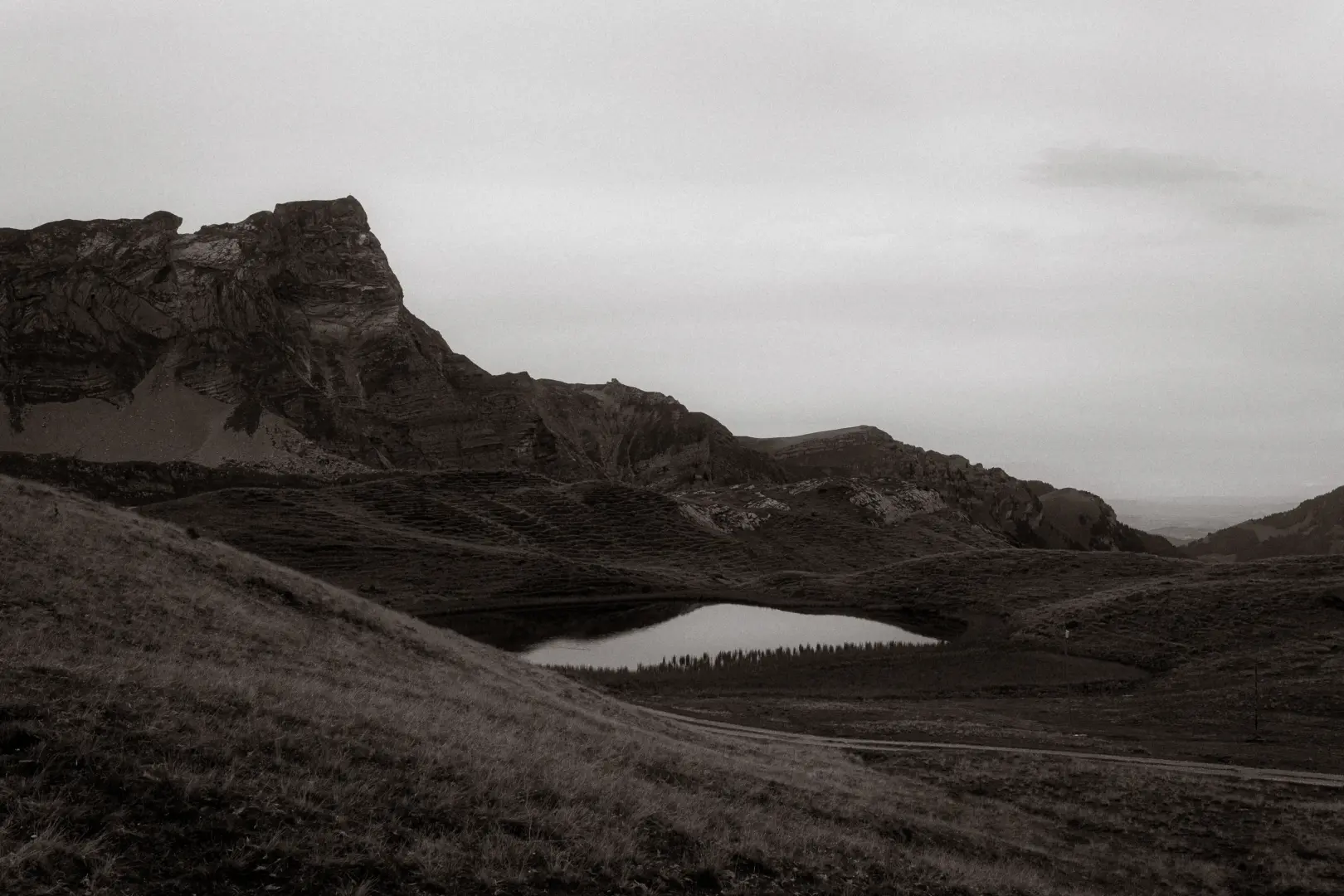 Ein kinematischer Hochzeitsfotograf in der Schweiz hält die dramatische Berglandschaft mit einem ruhigen Bergsee in Schwarz-Weiß fest, umgeben von zerklüfteten Felsformationen und einer weiten, melancholischen Alpenkulisse.