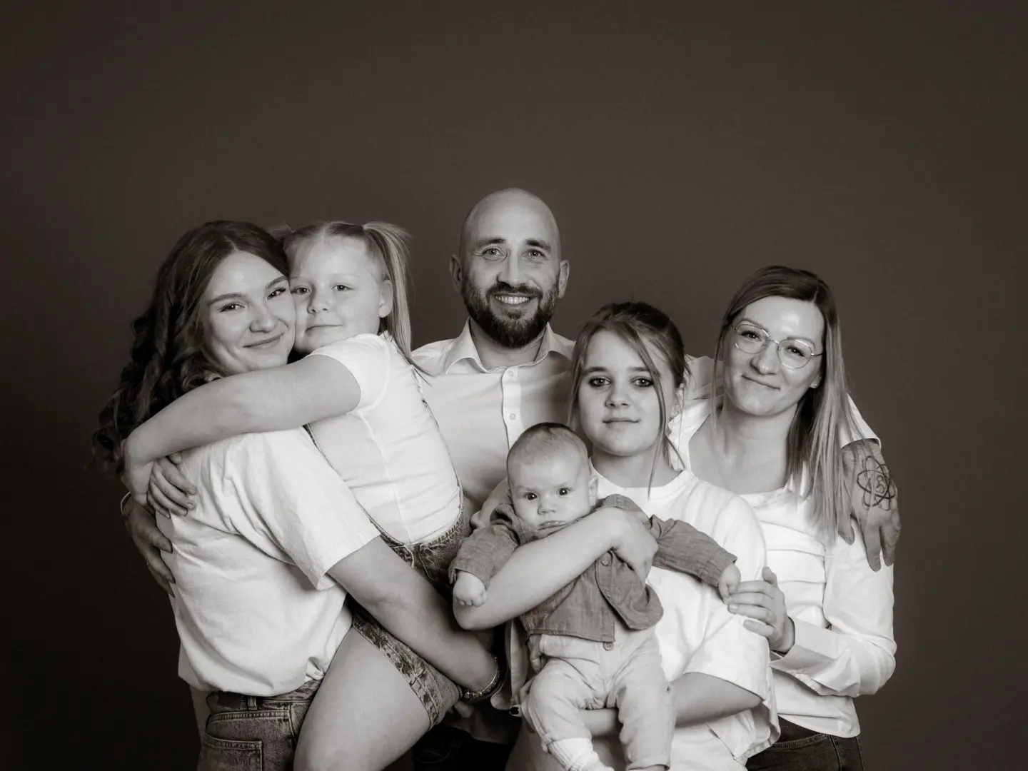 Eine glückliche Großfamilie mit einem Baby posiert gemeinsam vor einem schlichten Hintergrund im Fotostudio in Schwerin. Die Eltern und ihre vier Kinder strahlen in die Kamera, während sie sich liebevoll im Arm halten. Professionelle Familienfotos in Schwerin für bleibende Erinnerungen.