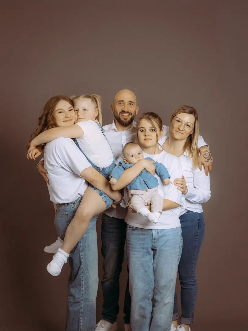 Eine glückliche Familie posiert vor einem neutralen Hintergrund in einem Fotostudio in Schwerin. Die Eltern halten ihre Kinder im Arm, alle tragen weiße T-Shirts und blaue Jeans. Das professionelle Familienfoto strahlt Wärme und Zusammenhalt aus.
