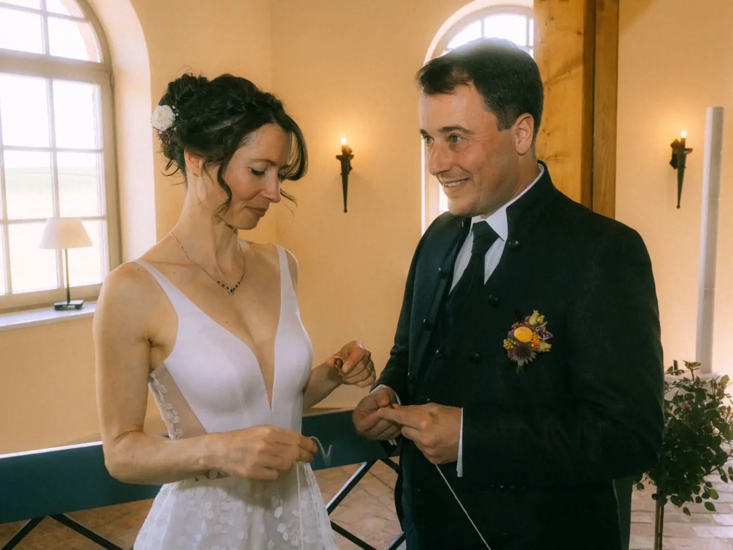 Ein Brautpaar tauscht während der Zeremonie liebevoll die Ringe. Die Braut trägt ein weißes Hochzeitskleid, der Bräutigam einen eleganten schwarzen Anzug mit Ansteckblume. Eine emotionale Aufnahme von einem Hochzeitsfotograf in Schwerin und MV in einer hellen, festlichen Location.