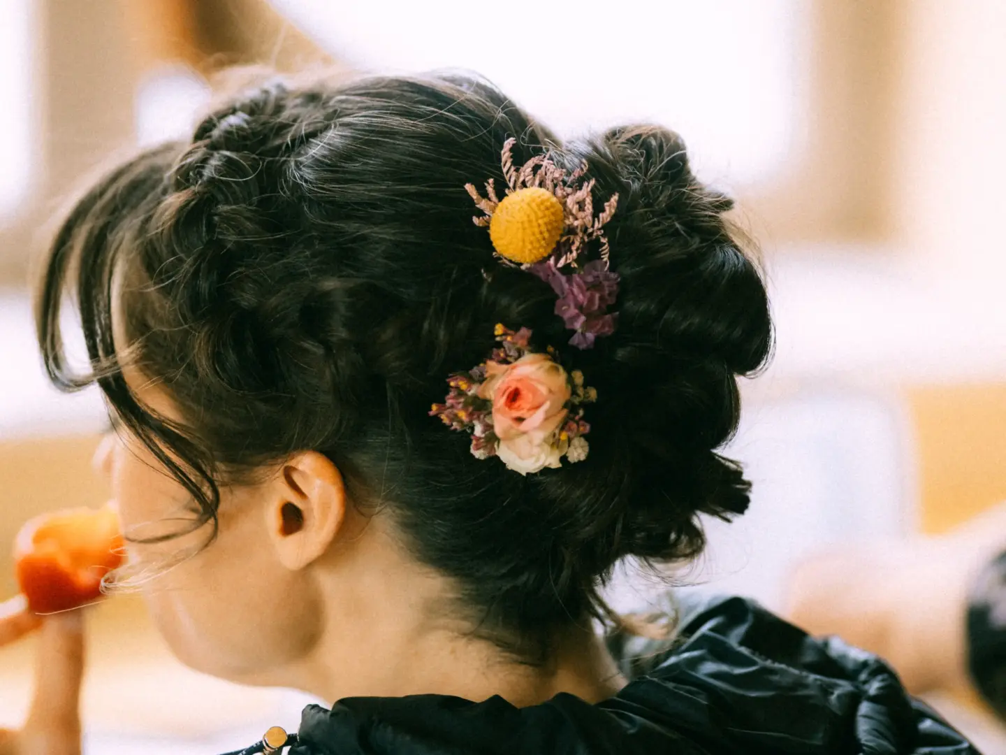 Eine Braut mit kunstvoll hochgesteckter dunkler Frisur, verziert mit getrockneten Blumen in Gelb und Rosa, eingefangen von einem Hochzeitsfotograf in Schwerin und MV. Die Aufnahme zeigt die elegante Detailansicht der Brautfrisur in einer weichen, natürlichen Lichtstimmung.