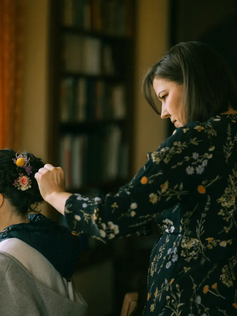 Eine Stylistin steckt einer Braut zarte Trockenblumen in die Hochsteckfrisur, während sie sich konzentriert auf das Styling vorbereitet. Die intime Szene fängt die Vorfreude ein, festgehalten von einem Hochzeitsfotograf in Schwerin und MV.