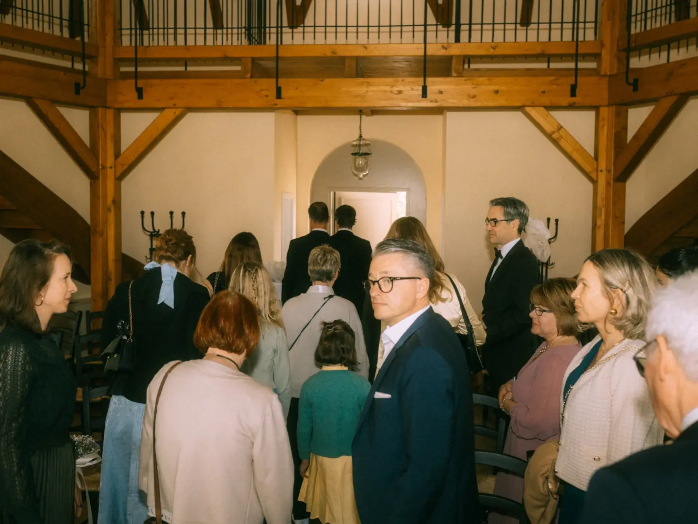 Gäste bei einer Hochzeitsfeier in einem rustikalen Saal mit Holzbalken. Die Menschen stehen in einer Schlange, während ein Hochzeitsfotograf in Schwerin und MV die natürliche Stimmung und die festliche Atmosphäre dieser Zusammenkunft einfängt.