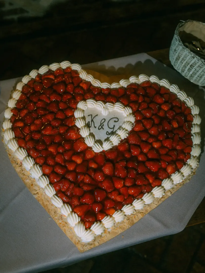 Herzförmige Hochzeitstorte, üppig belegt mit frischen Erdbeeren und verziert mit Sahnetupfern. In der Mitte befindet sich eine helle Fläche mit der Inschrift „K & G“. Ein stimmungsvolles Detail für den Hochzeitsfotograf in Schwerin und MV.