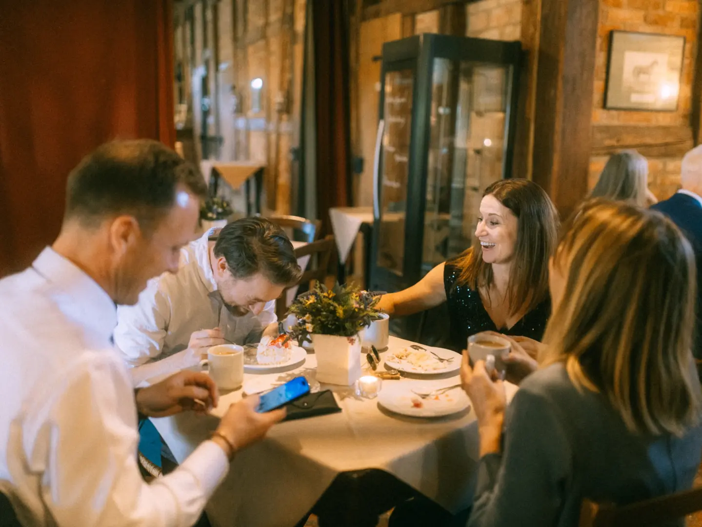 Vier Freunde sitzen an einem runden Tisch in einem gemütlichen Restaurant, lachen und genießen ihr Dessert. Die warme Atmosphäre unterstreicht diesen besonderen Moment, eingefangen von einem Hochzeitsfotograf in Schwerin und MV, während sie gemeinsam Zeit verbringen.