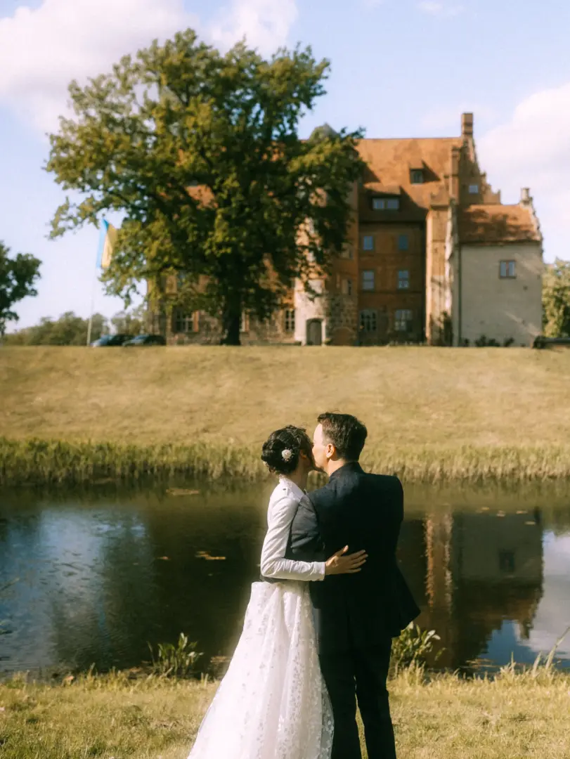 Ein Brautpaar küsst sich romantisch vor einem historischen Schloss mit Wassergraben. Das Paar steht im Profil, die Braut trägt ein weißes Kleid und der Bräutigam einen dunklen Anzug. Diese stimmungsvollen Pärchenfotos in Schwerin fangen die Eleganz einer Hochzeit in MV perfekt ein.