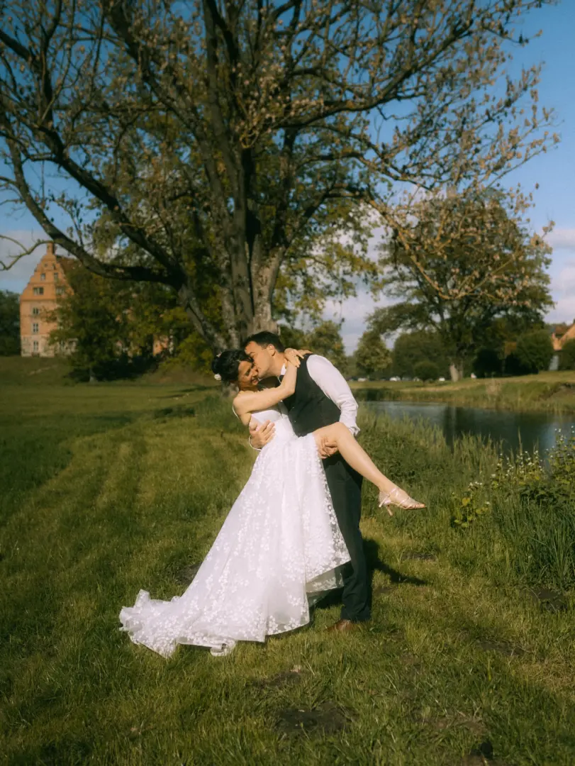 Ein Brautpaar in einer romantischen Pose, bei der der Bräutigam die Braut auf einer grünen Wiese vor einem Schloss und einem See küsst. Diese Aufnahme einer Lovestory zeigt die emotionale Verbundenheit und wurde von einem Lovestory Fotograf in Schwerin und MV festgehalten.