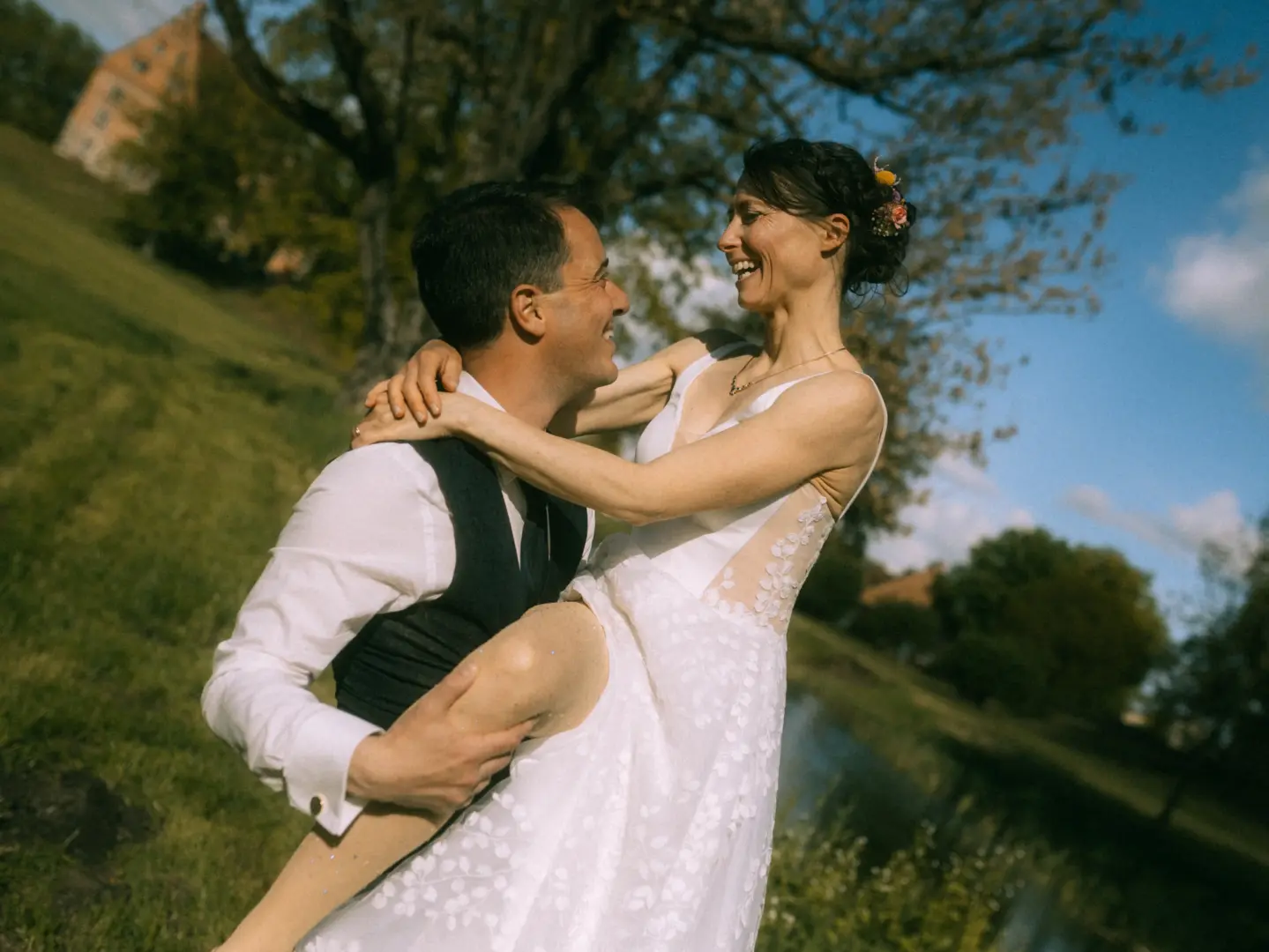 Ein glückliches Brautpaar lacht herzlich, während der Bräutigam die Braut in seinem Hochzeitsanzug vor einer malerischen Schlosskulisse hochhebt. Diese romantische Aufnahme unterstreicht die Arbeit als Hochzeitsfotograf in Schwerin und MV.