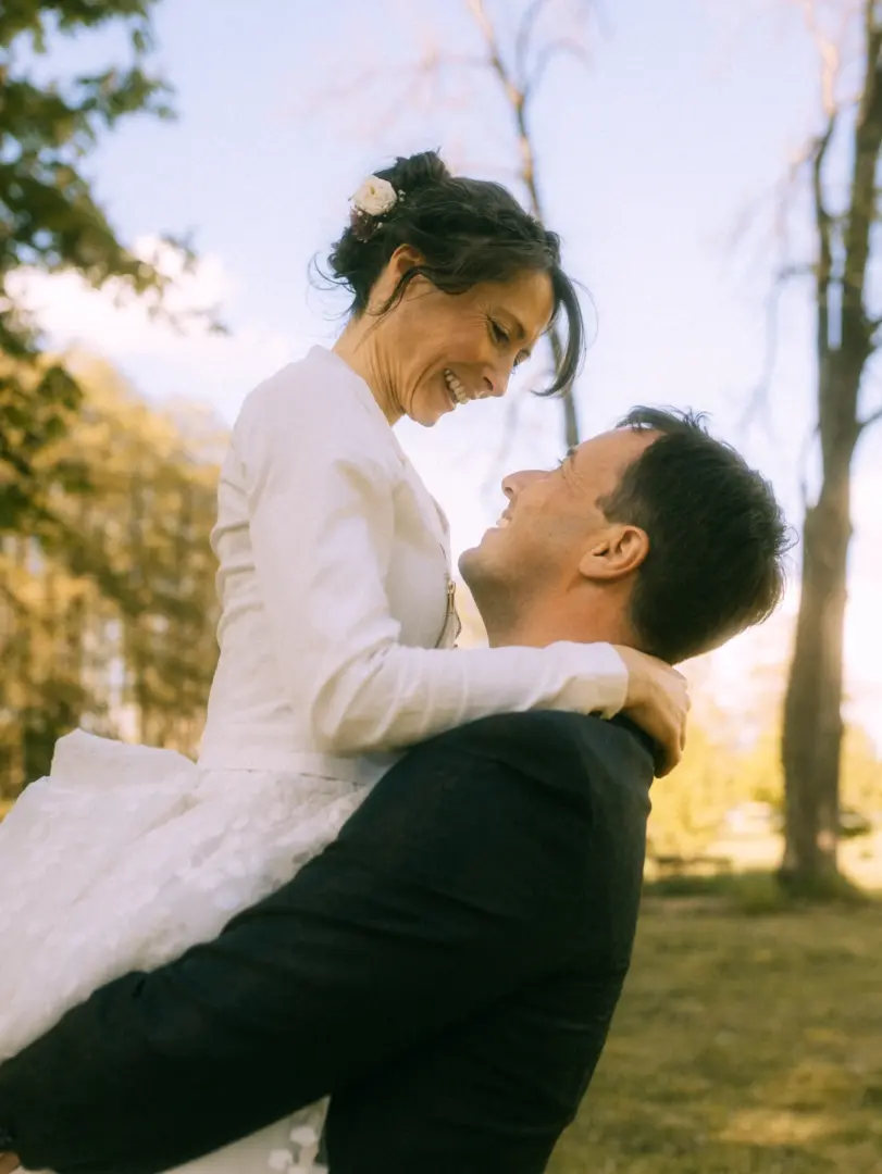 Ein glückliches Brautpaar in einer innigen Umarmung: Der Bräutigam hebt seine lachende Braut im weißen Hochzeitskleid vor einer sonnendurchfluteten Waldkulisse hoch. Ein romantischer Moment, eingefangen von einem Hochzeitsfotograf in Schwerin und MV.