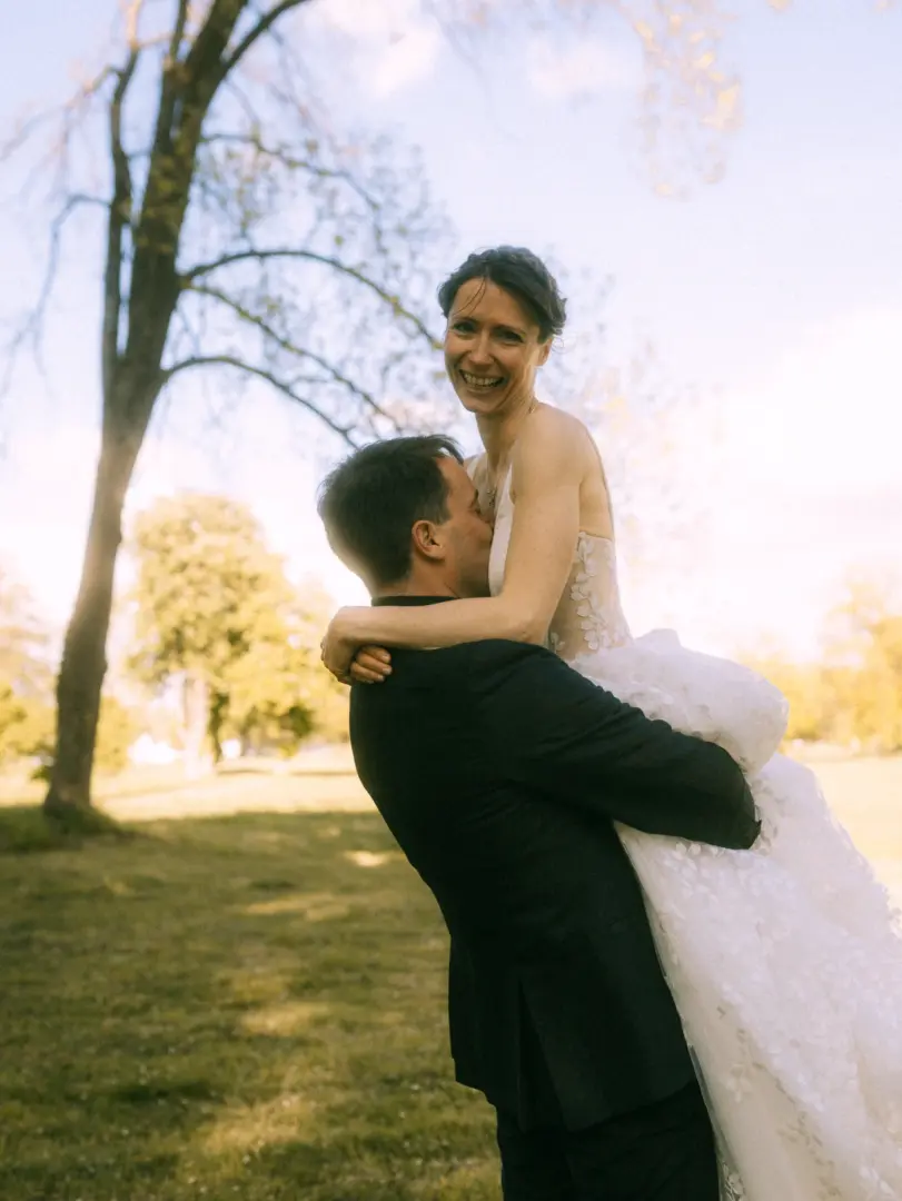 Ein glückliches Brautpaar bei einem romantischen Fotoshooting im Grünen: Der Bräutigam hebt seine Braut im weißen Spitzenkleid hoch, während sie strahlend in die Kamera blickt. Ein stimmungsvoller Moment, eingefangen von einem Hochzeitsfotograf in Schwerin und MV.