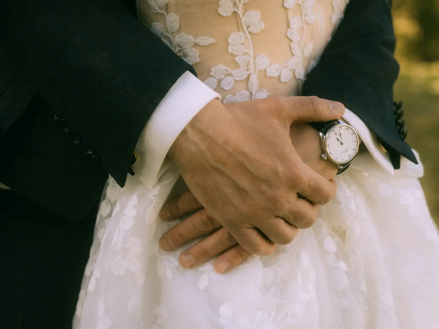 Nahaufnahme eines Bräutigams, der seine Braut in einem weißen Spitzenkleid zärtlich umschlingt. An seinem Handgelenk trägt er eine elegante Armbanduhr. Ein romantischer Moment, festgehalten von einem Hochzeitsfotograf in Schwerin und MV.