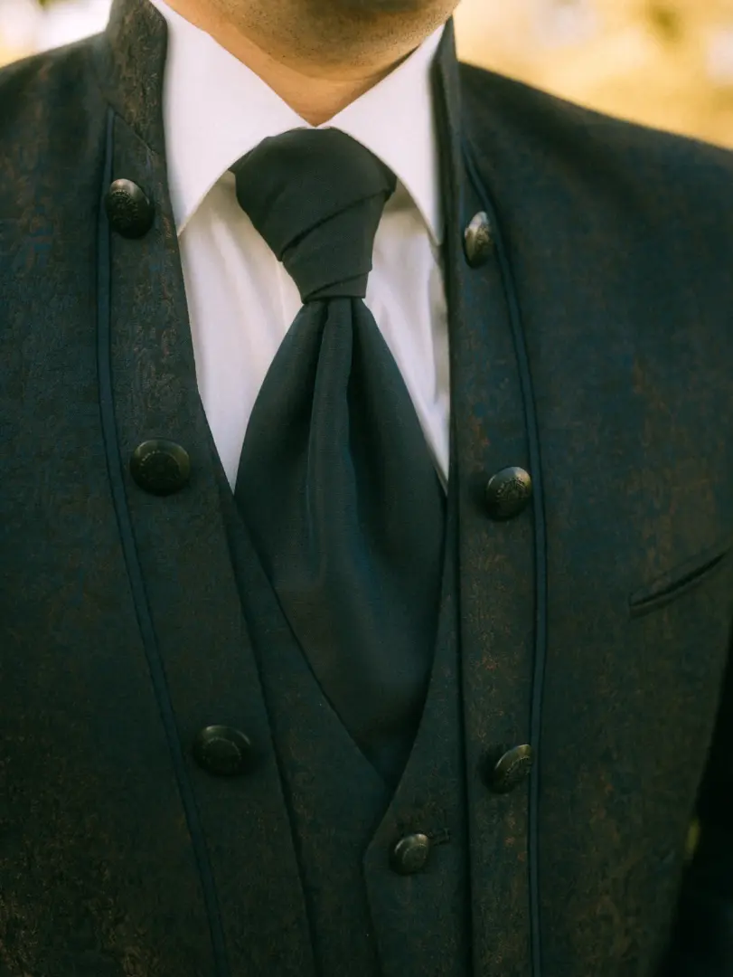 Nahaufnahme eines Bräutigams in einem eleganten, dunkelblauen Anzug mit Paisley-Muster, weißem Hemd und einer schwarzen Krawatte. Die feinen Details der Knöpfe und des Stoffes unterstreichen den festlichen Stil. Hochzeitsfotograf in Schwerin und MV.