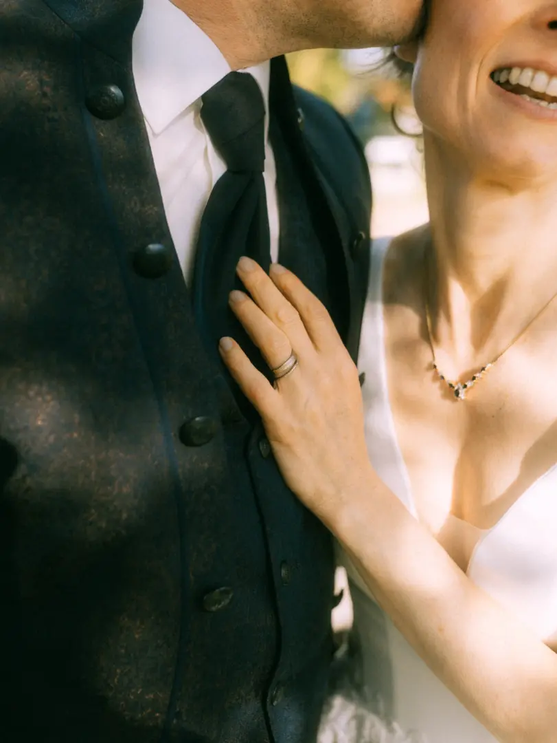 Nahaufnahme eines glücklichen Brautpaares: Die Braut legt ihre Hand sanft auf den dunklen Anzug des Bräutigams, während dieser ihr einen Kuss gibt. Ein romantischer Moment, festgehalten von einem Hochzeitsfotograf in Schwerin und MV.