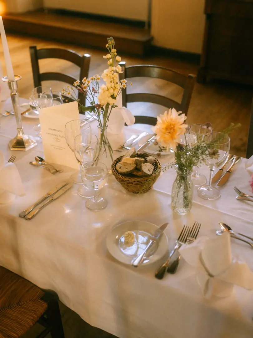 Festlich gedeckter Hochzeitstisch mit Blumenarrangements, Weingläsern und einem Brotkorb. Auf der Menükarte steht „Hochzeitsfest Kathrin & Guido“. Stilvolle Tischdekoration für eine Feier, fotografiert von einem Hochzeitsfotograf in Schwerin und MV.