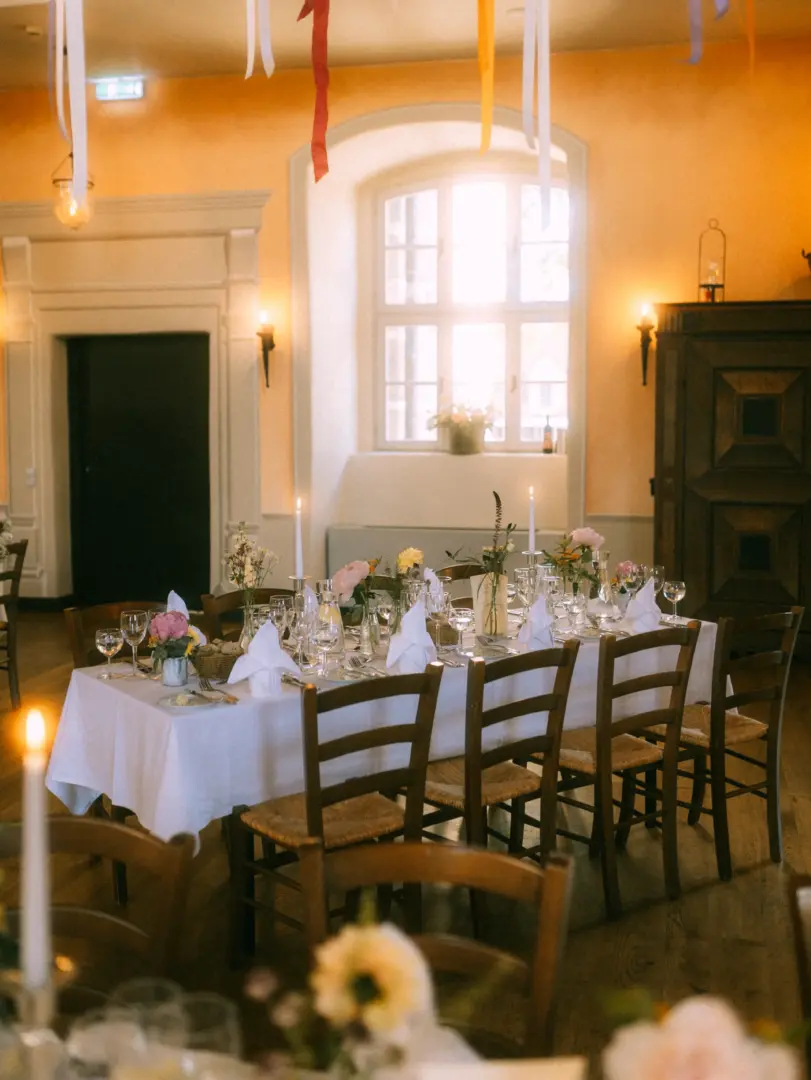 Festlich gedeckter Hochzeitstisch in einem historischen Saal mit warmem Licht, eleganten Blumenarrangements und hängenden Bändern. Stimmungsvolle Hochzeitsdekoration in einem Schlossambiente, eingefangen von einem Hochzeitsfotograf in Schwerin und MV.