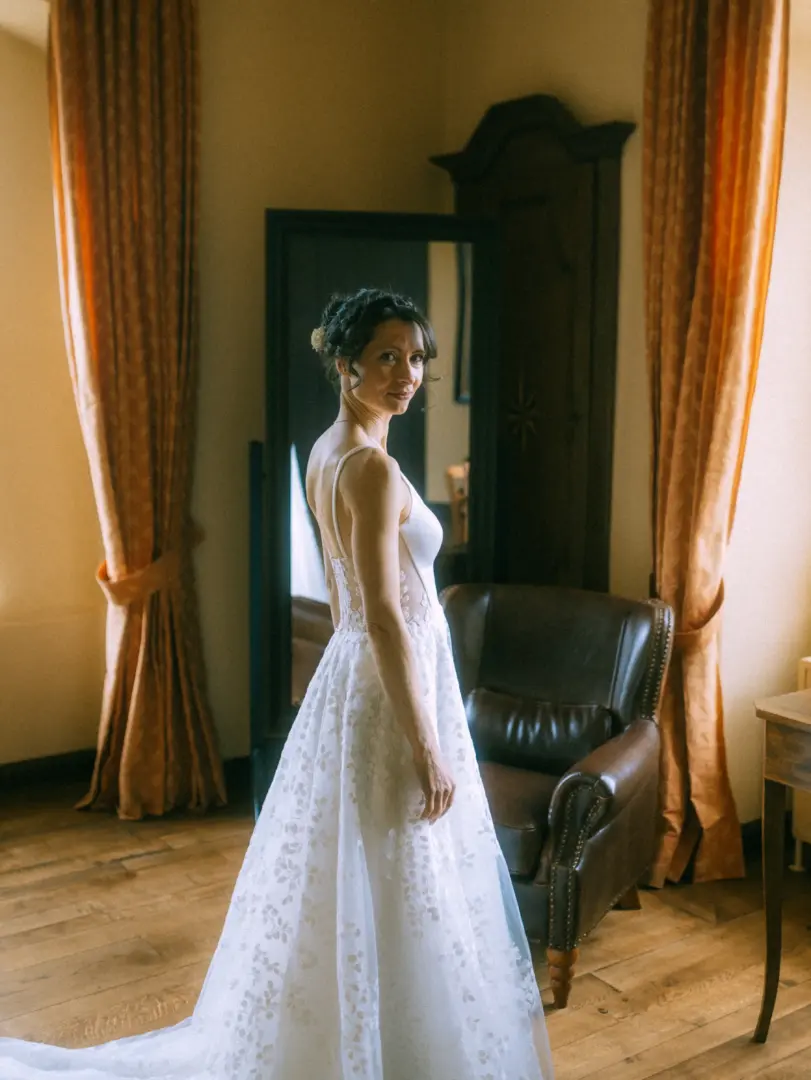Eine Braut in einem eleganten, floral bestickten Brautkleid mit Spaghettiträgern blickt sanft über die Schulter in die Kamera. Die Aufnahme im warmen Licht eines klassischen Zimmers unterstreicht die Arbeit als Hochzeitsfotograf in Schwerin und MV.