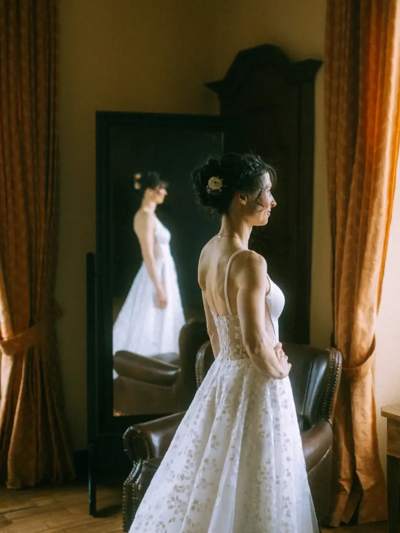 Eine Braut in einem eleganten, floral bestickten Hochzeitskleid betrachtet ihr Spiegelbild in einem antiken Spiegel. Die stimmungsvolle Szene in einem klassischen Raum unterstreicht die Arbeit als Hochzeitsfotograf in Schwerin und MV.