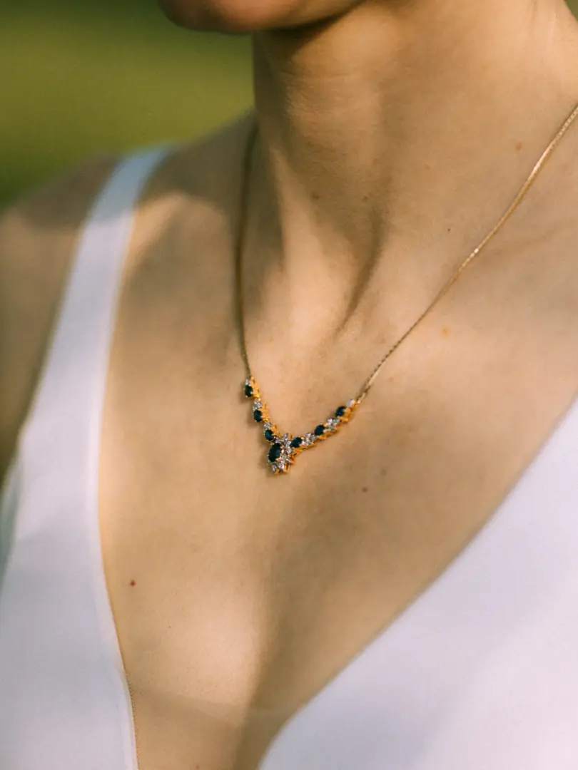 Eine elegante Braut trägt eine filigrane Goldkette mit Saphiren und Diamanten, die perfekt zu ihrem weißen Hochzeitskleid passt. Das detailreiche Schmuckstück setzt einen edlen Akzent bei diesem Hochzeitsfotograf in Schwerin und MV.