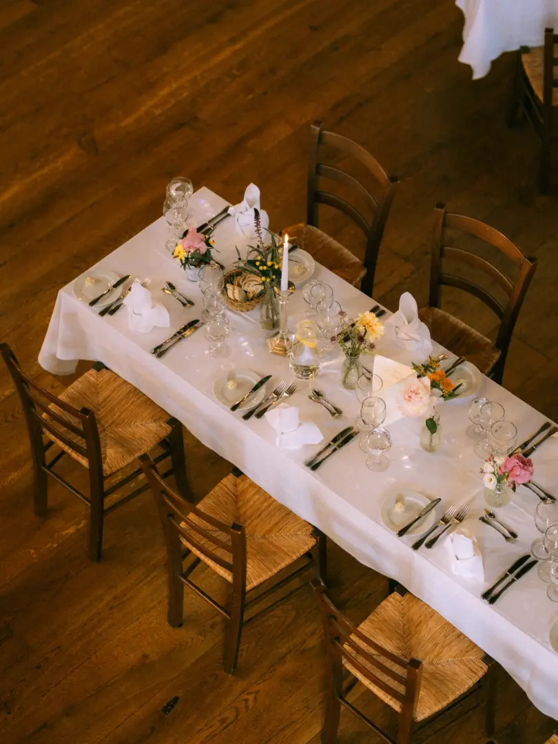Ein elegant gedeckter Hochzeitstisch in einer rustikalen Location mit Holzboden, geschmückt mit frischen Blumenarrangements, Kerzen und feinem Geschirr. Dieses stimmungsvolle Detailbild wurde von einem Hochzeitsfotograf in Schwerin und MV eingefangen.