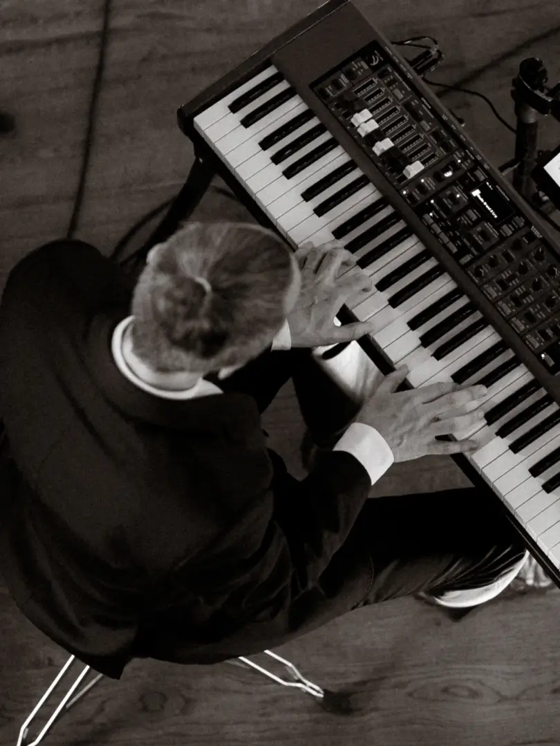 Ein Musiker in einem eleganten dunklen Anzug spielt konzentriert auf einem Nord Stage Keyboard. Die schwarz-weiße Aufnahme aus der Vogelperspektive zeigt seine Hände auf den Tasten, während er bei einer Veranstaltung auftritt. Professioneller Hochzeitsfotograf in Schwerin und MV.
