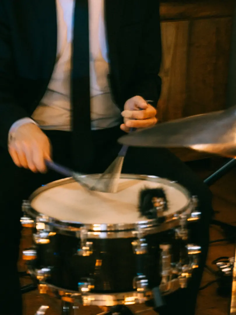 Ein Schlagzeuger in einem eleganten schwarzen Anzug spielt mit Besen auf einer Snare-Drum, eingefangen durch Ihren Hochzeitsfotograf in Schwerin und MV. Die dynamische Bewegung der Drumsticks und die stimmungsvolle Beleuchtung unterstreichen die musikalische Atmosphäre.