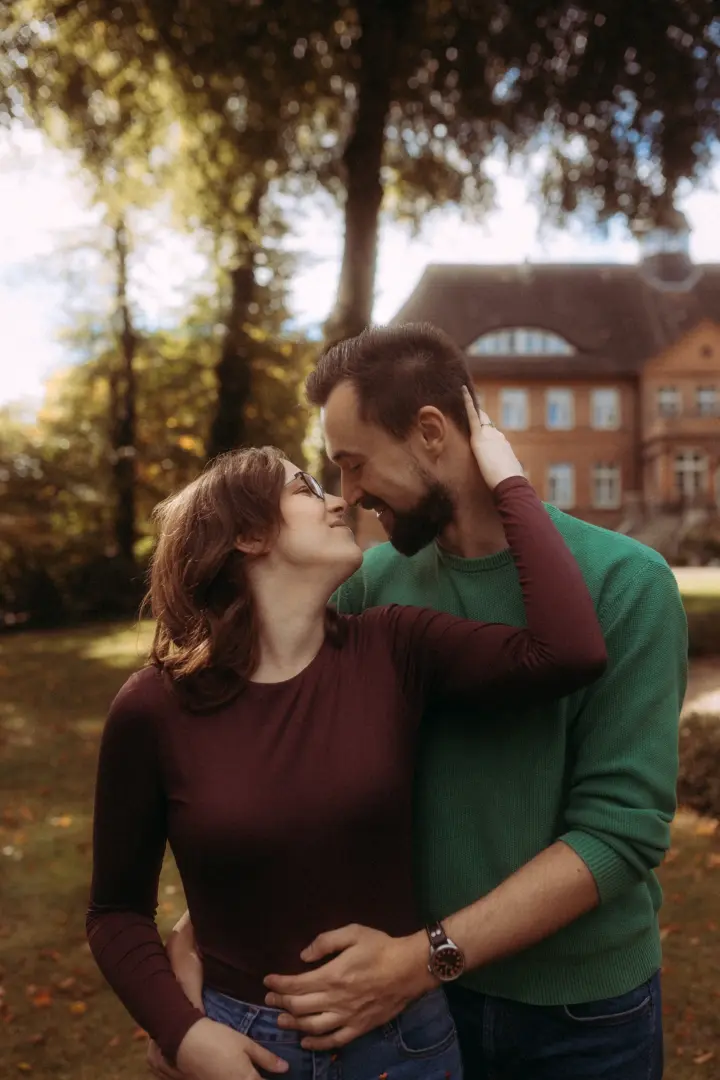 Ein verliebtes Paar blickt sich in einem herbstlichen Park zärtlich an, während der Mann die Frau liebevoll in den Armen hält. Die romantische Atmosphäre unterstreicht die Verbundenheit der beiden bei einem professionellen Shooting für Pärchenfotos in Schwerin.