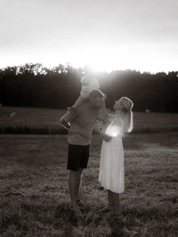 Ein glückliches Paar mit ihrem kleinen Kind auf den Schultern bei einem Spaziergang im goldenen Licht der Abendsonne auf einem Feld. Die stimmungsvolle Aufnahme zeigt eine liebevolle Familienzeit als professionelle Familienfotos in Schwerin.
