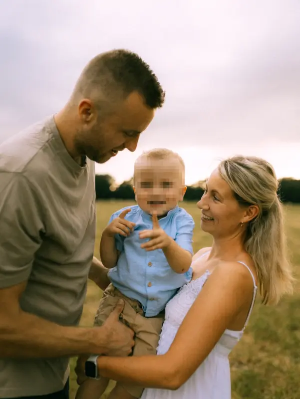 Eine junge Familie genießt einen sonnigen Moment auf einer Wiese, während die Eltern liebevoll auf ihr Kind schauen. Das authentische Familienfoto fängt die Verbundenheit im Freien ein. Professioneller Fotograf für Familien in Schwerin für natürliche Familienfotos in Schwerin.