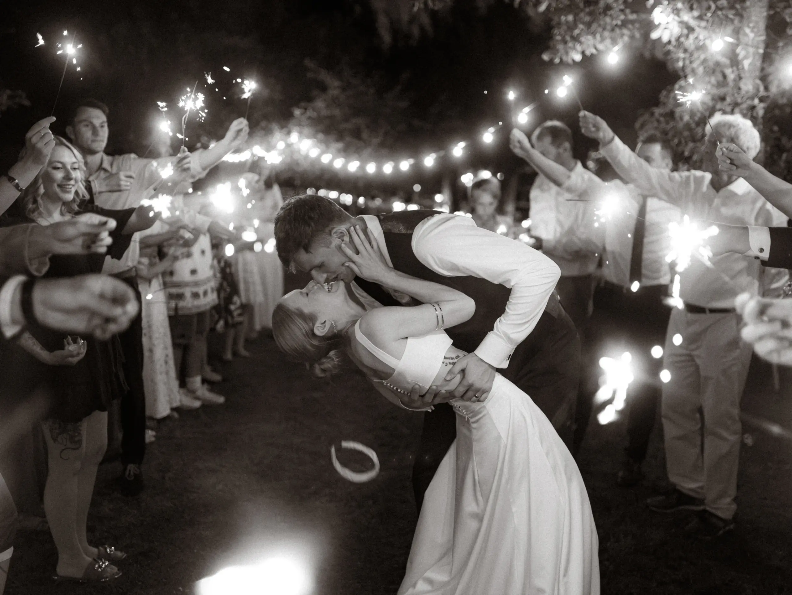 Ein frisch vermähltes Brautpaar küsst sich innig bei einem romantischen Funkenregen-Spalier ihrer Hochzeitsgäste in der Nacht. Das stimmungsvolle Foto fängt diesen besonderen Moment als Hochzeitsfotograf in Schwerin und MV perfekt ein.