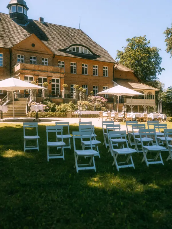 Weiße Klappstühle stehen für eine Hochzeitszeremonie für eine freie Trauung beim Schloss Basthorst bereit. Hochzeitsfotograf in Crivitz & Basthorst.